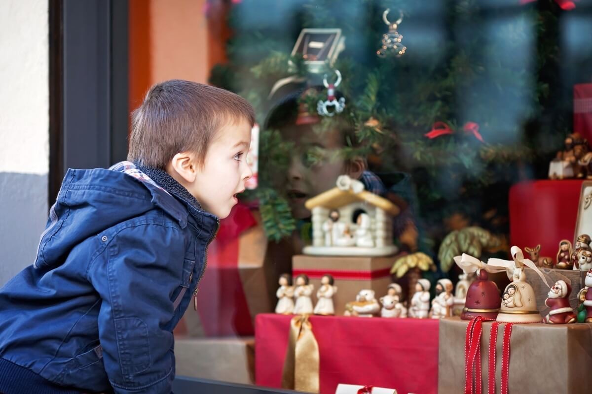 Sweet little boy, looking through a window in shop