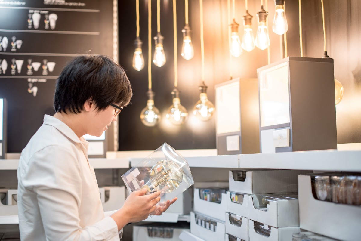 Young Asian man choosing package of electrical light bulb, furniture home decoration shopping concept